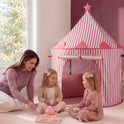A woman and two young girls sit on the floor having a tea party next to a pink and white striped Starry Indoor Play Tent for Toddlers.