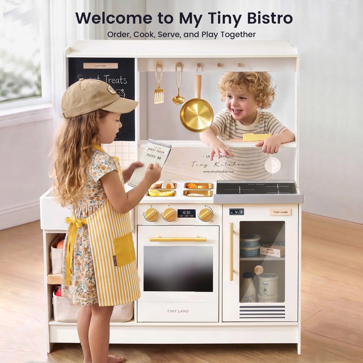 A young girl in an apron holds a menu for a boy engaged in role-play inside a BistroSwitch 2-in-1 Play Kitchen & Bistro.