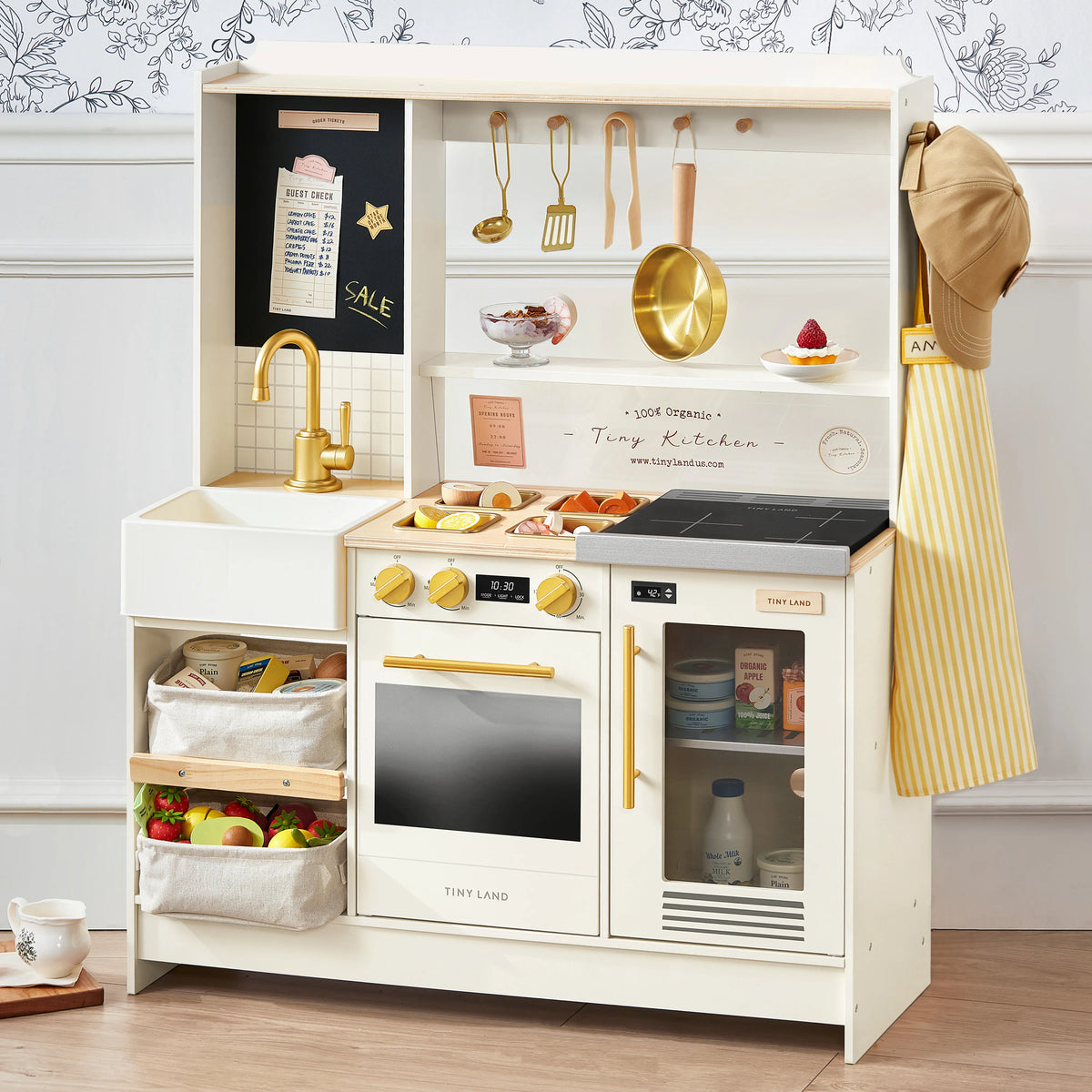 Cream-colored BistroSwitch 2-in-1 Play Kitchen & Bistro featuring a sink, oven, stovetop, and shelves stocked with play food, utensils, and storage baskets.
