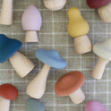 A Mushroom Mix & Match Sorting Toy (24 pc) set featuring an assortment of colorful wooden mushrooms with matte caps arranged on a tan grid-patterned surface.
