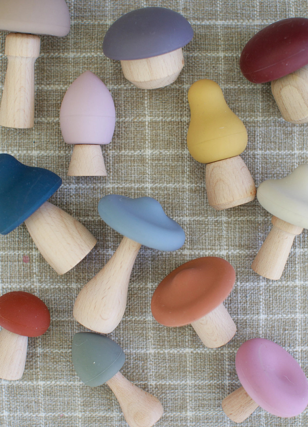 A Mushroom Mix & Match Sorting Toy (24 pc) set featuring an assortment of colorful wooden mushrooms with matte caps arranged on a tan grid-patterned surface.