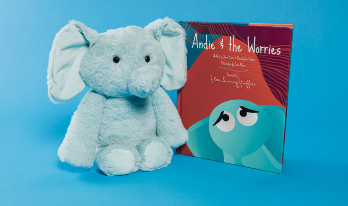 A mint-green Andie the Elephant Plush sitting next to the children’s book Andie & the Worries.