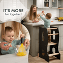 A toddler stands on the Stable Montessori Tower: Wooden Growing Chair - Grey at a kitchen counter, reaching toward a smiling woman. Inset shows the toddler whisking eggs in a glass bowl with help. Text reads, IT’S MORE fun together! The Stable Montessori Tower makes every little chef a true kids kitchen helper.