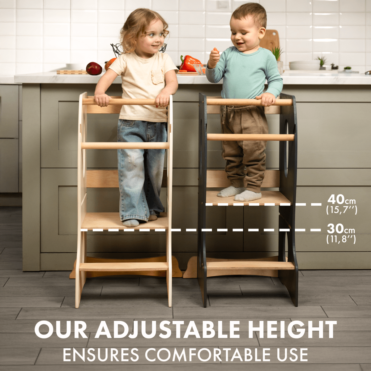 Two young children stand on separate Stable Montessori Tower: Wooden Growing Chair - Grey stools of different heights in a kitchen, demonstrating adjustable height levels at 40 cm and 30 cm. Text reads: Our Stable Montessori Tower offers comfortable, adjustable use—making it the ideal kids kitchen helper for every growing chef.