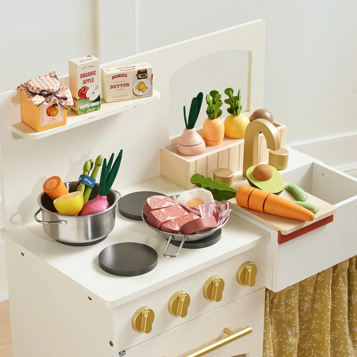 A white toy kitchen set with a pretend fridge stocked with a Pretend Dairy Play Pack and various wooden vegetables, meat, and juice.