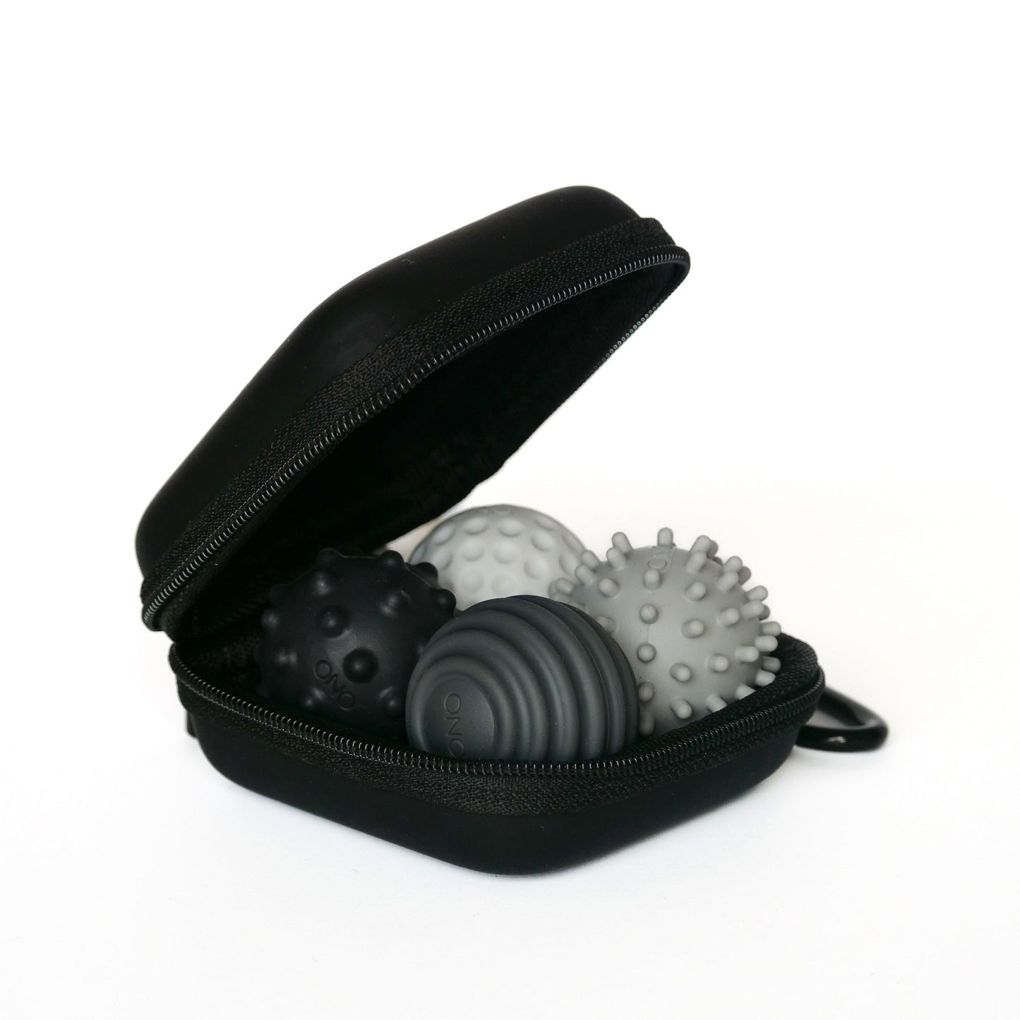 An open graphite Signets case displays three textured massage balls, each with unique patterns and raised bumps designed to enhance focus and offer a soothing fidgeting experience.