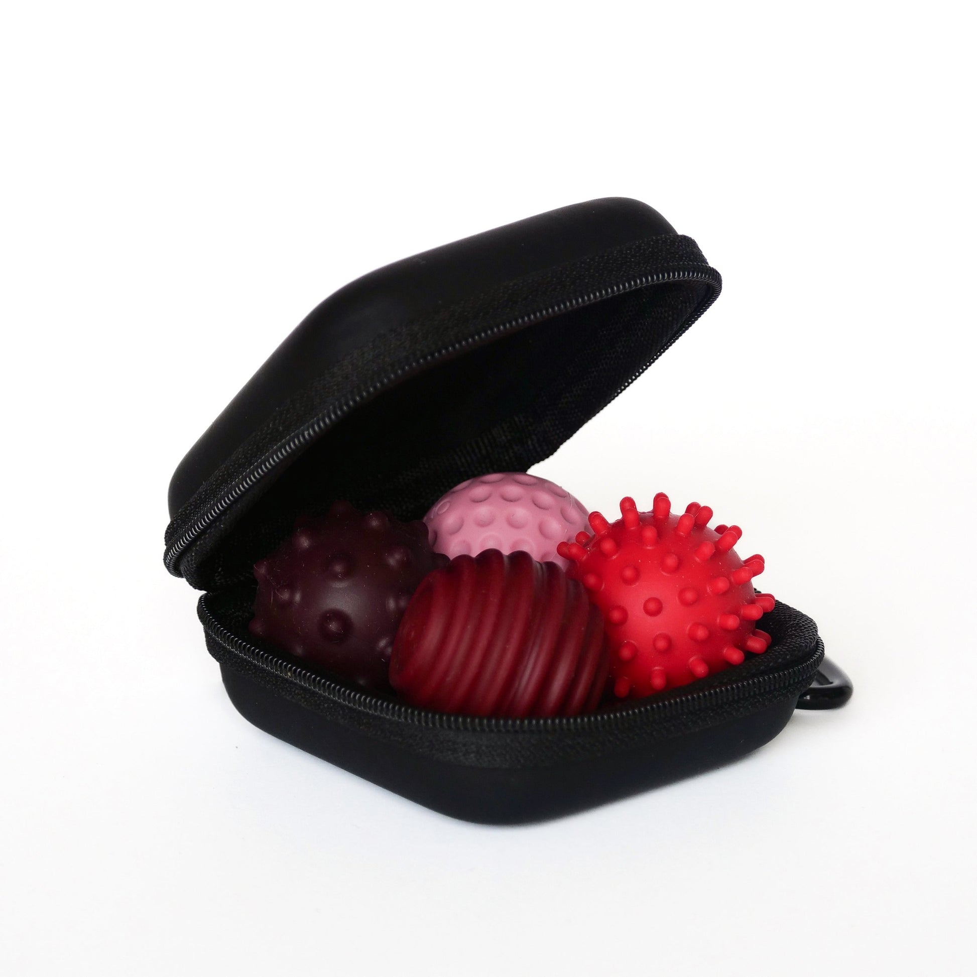 An open Signets case in Ruby displays four textured balls in shades of red and pink, each with unique raised patterns for satisfying fidgeting. The case is black with a zipper, shown against a plain white background.