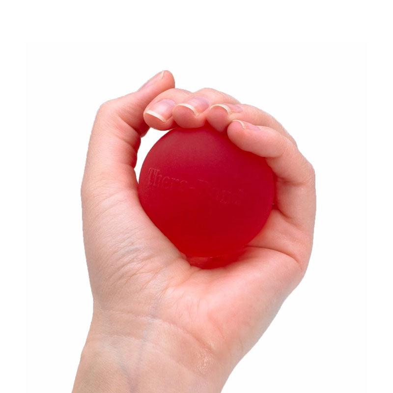 A hand squeezing a red, round THERABAND Hand Exerciser Grip Ball to improve grip strength.