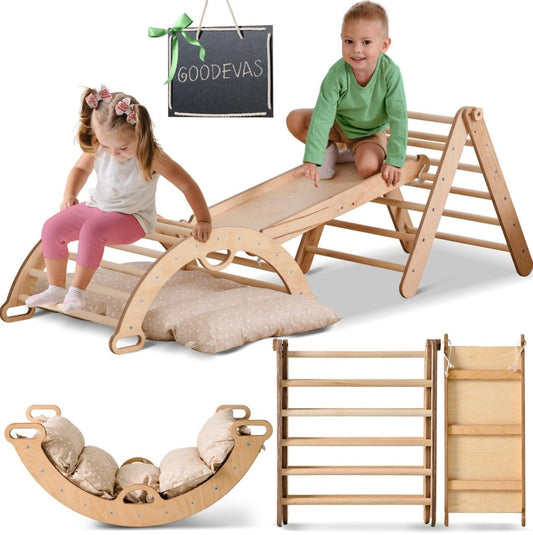 Two young children play on a beige Pikler Triangle Set for Toddlers, which includes a triangle ladder, climbing arch, slide board, and cushion. The pieces are arranged creatively with a Goodevas chalkboard sign visible.