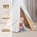 A young child peeks out from the Play Tent Cover with Mat for Climbing Triangle Ladder, cozily set up beside a Montessori triangle ladder. Nearby text highlights: SAFE SPACE, CREATIVITY, and PHYSICAL GROWTH. Soft neutral curtains and carpeting provide a calming backdrop.