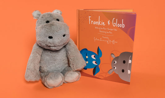 A grey Frankie the Hippo Plush + Book sits next to a children’s picture book.