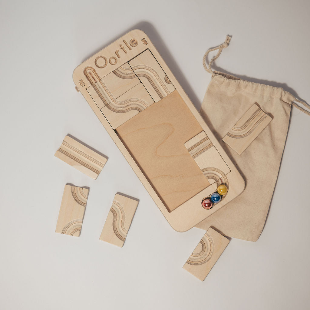 Oortle – Mini Wooden Marble Run Puzzle featuring three colorful marbles, several separate wooden track tiles, and a cloth drawstring bag.