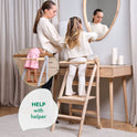 An adult and a child stand at a wooden vanity using the Toddler Tower: Foldable Step Stool for Toddlers - Gray. An inset highlights a close-up of the child’s feet on the step. Text reads, HELP with helper.