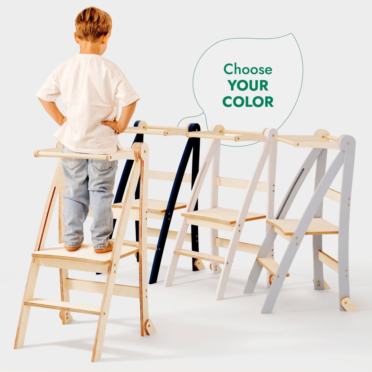 A young child stands on a Toddler Tower: Foldable Step Stool for Toddlers - Gray, with three stylish color options shown side by side. A speech bubble above the towers reads Choose YOUR COLOR. This foldable toddler step stool blends safety and style—perfect for supporting your little one’s everyday adventures.