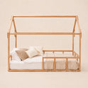 A Twin Size Montessori House Bed for Kids with Fence, featuring a minimalist house-shaped frame crafted from solid beech wood with a low base, no roof or walls, displayed with a mattress, neutral bedding, and several pillows against a plain beige background.