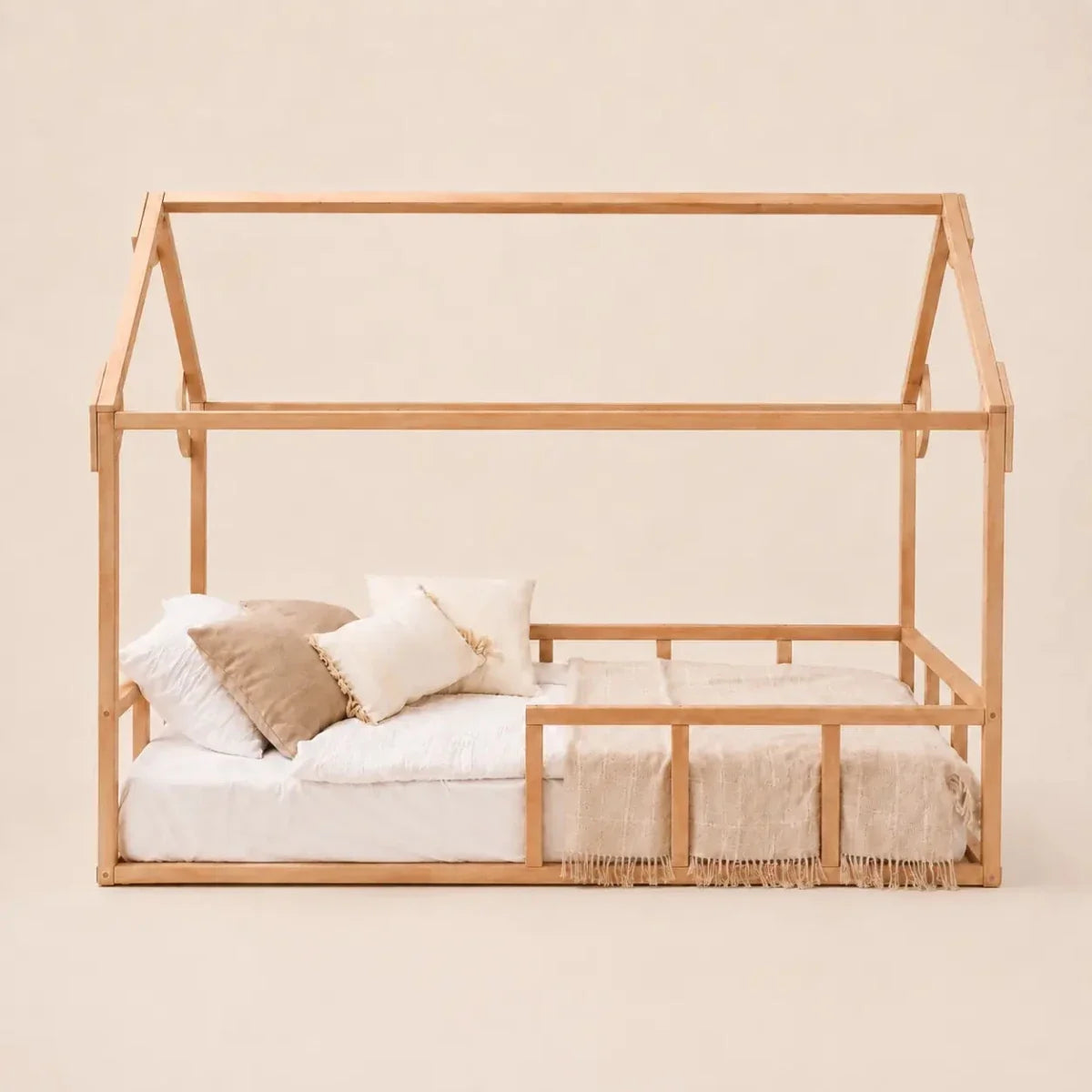 A Twin Size Montessori House Bed for Kids with Fence, featuring a minimalist house-shaped frame crafted from solid beech wood with a low base, no roof or walls, displayed with a mattress, neutral bedding, and several pillows against a plain beige background.