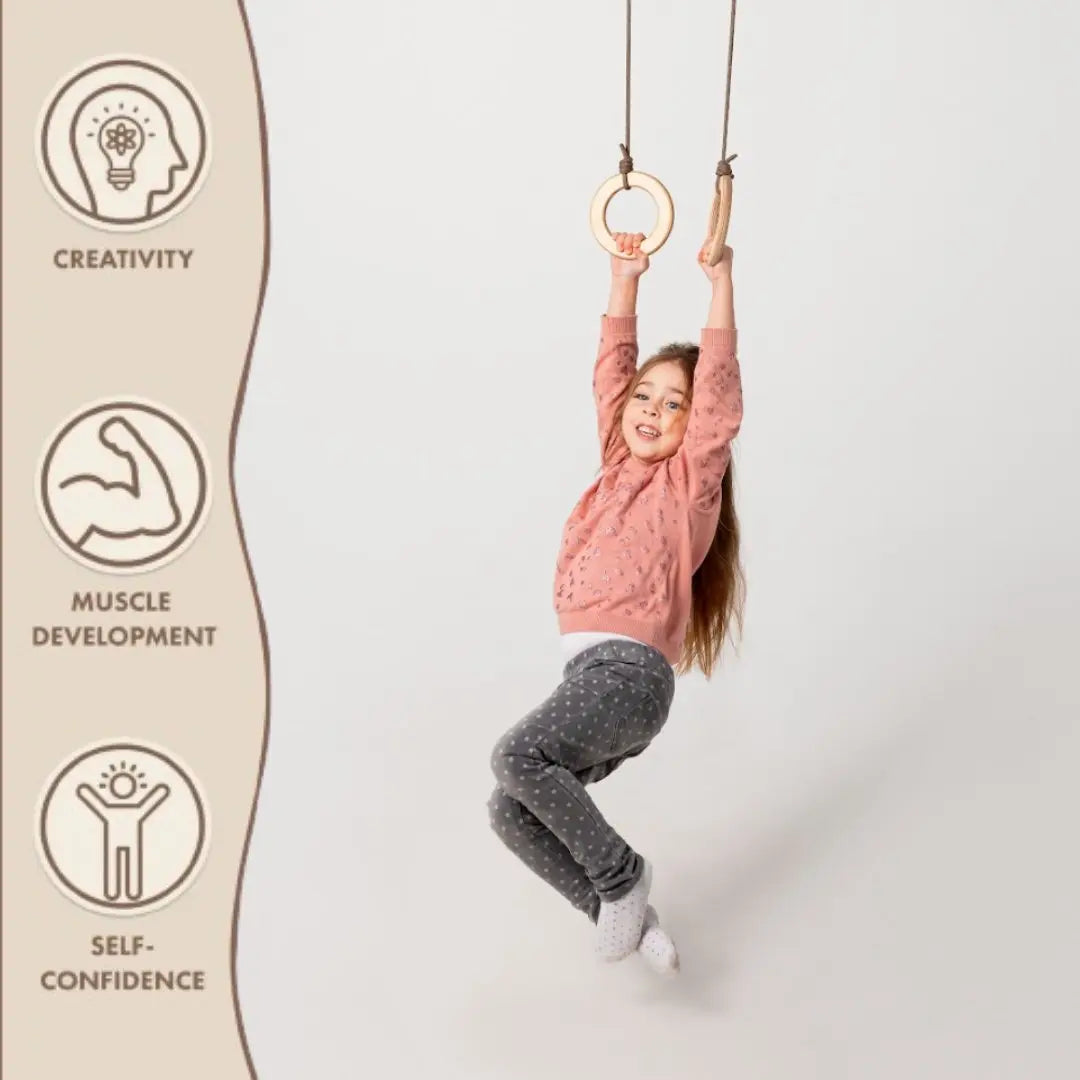 A happy child plays on Wooden gymnastic rings for kids, highlighting the enjoyable approach to children’s fitness. To the left, three icons symbolize creativity, muscle development, and self-confidence. The plain, light background keeps the emphasis on physical growth and activity.