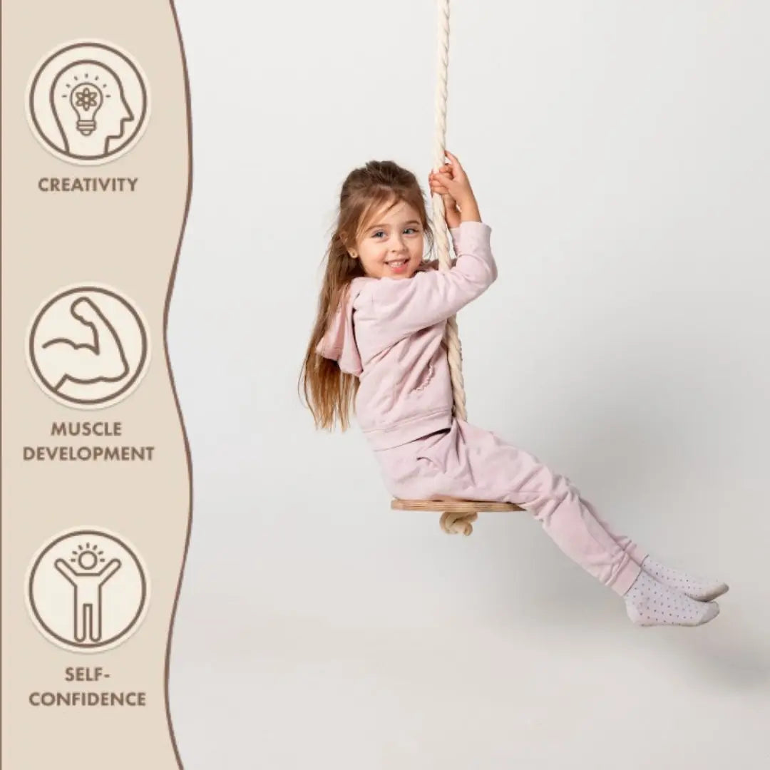 A young girl dressed in pink smiles as she swings on a Wooden Rope Swing for Kids. Icons and text on the left highlight its benefits: Creativity, Muscle Development, and Self-Confidence. Ideal for both indoor gym fun and outdoor play.