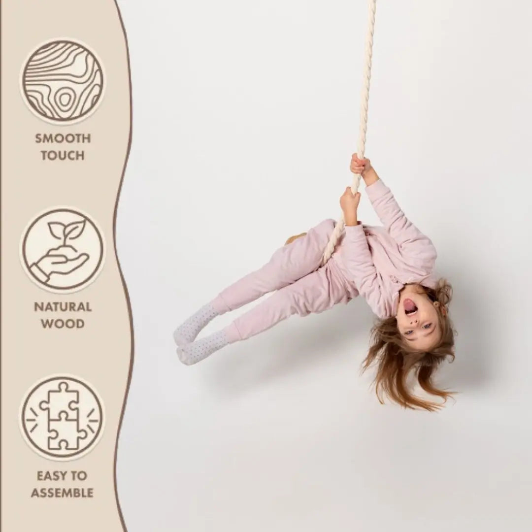 A child in pink pajamas swings on the Wooden rope swing for kids against a white background. Icons to the left read: Smooth Touch, Natural Wood, and Easy to Assemble—making it perfect for an indoor gym or outdoor play.